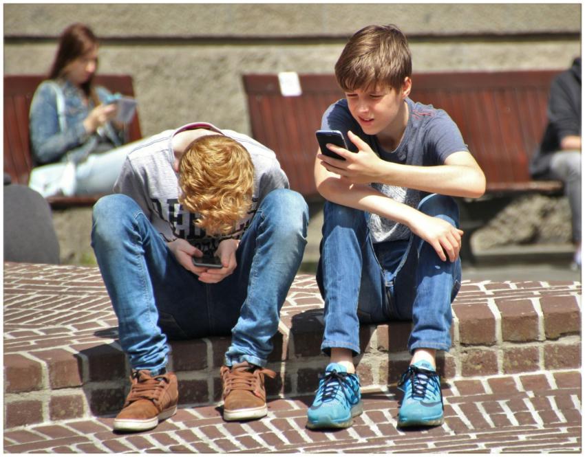 Two teenagers seated outdoors, focused on their sm