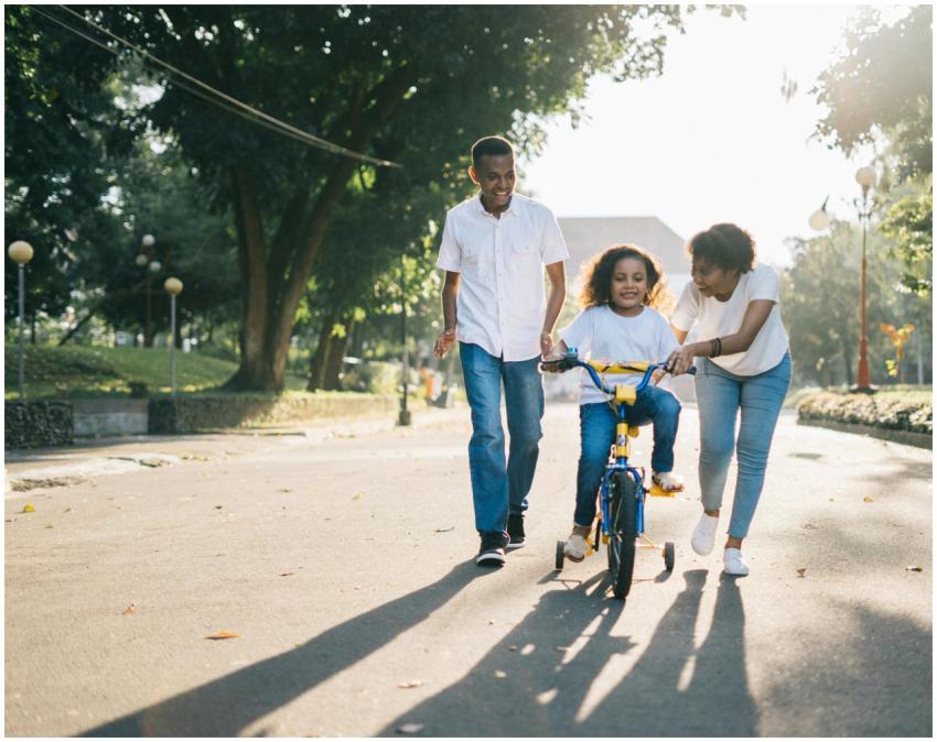 Happy family teaching their child to cycle on a su