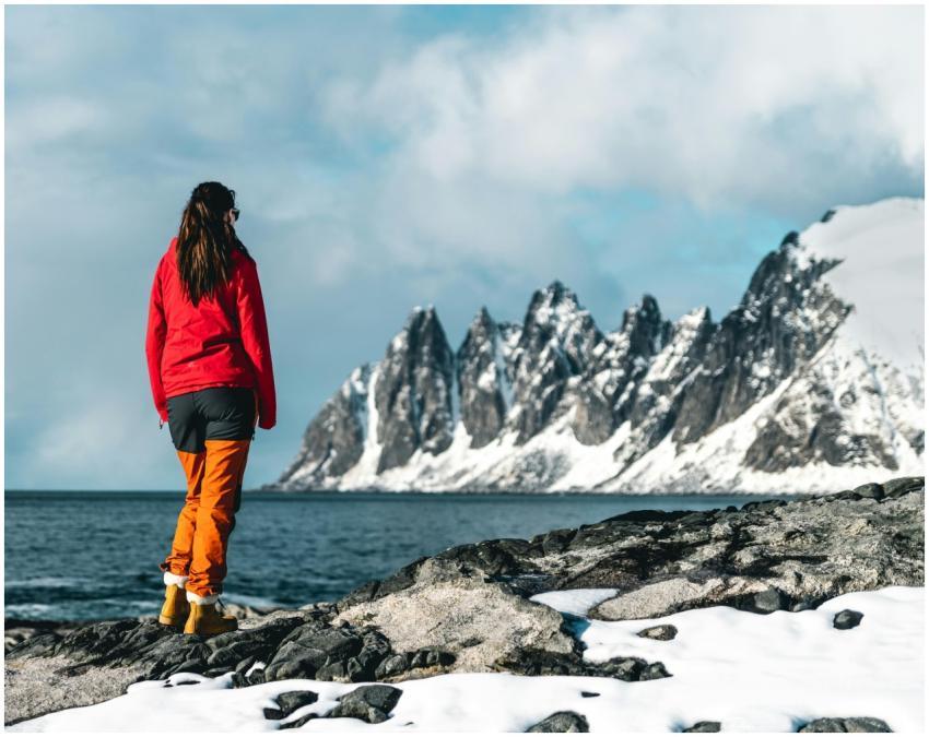 Woman in red jacket hiking in snowy mountains by t