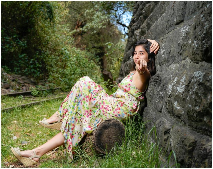 Young woman in floral dress relaxing against stone