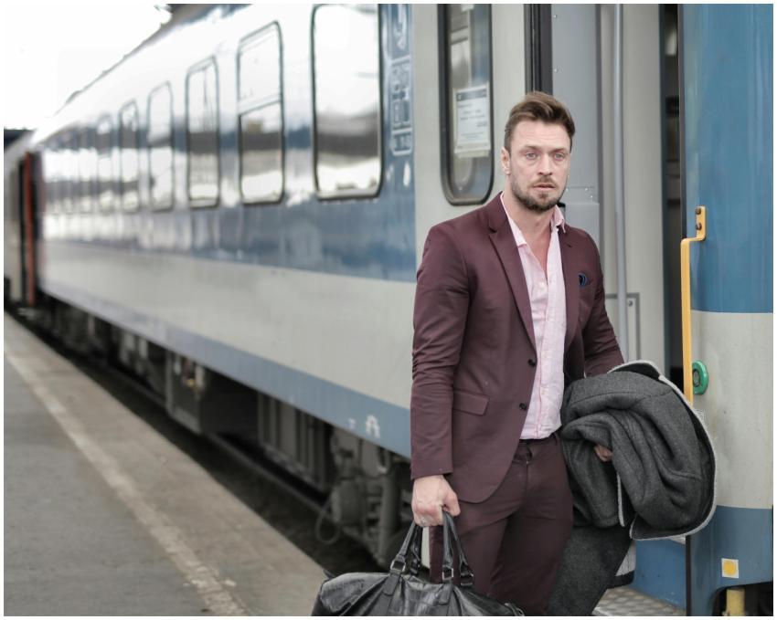 Man in suit exiting a passenger train, holding a c