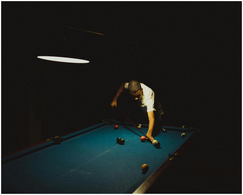 A focused player takes aim at a billiard table ill