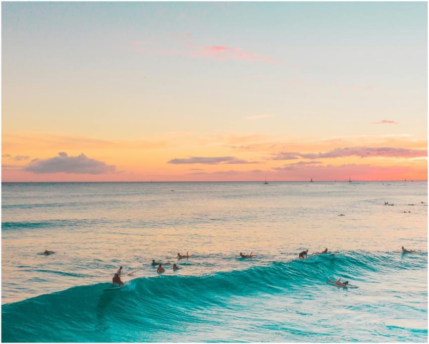 Surfers catch waves under a vibrant sunset sky, cr