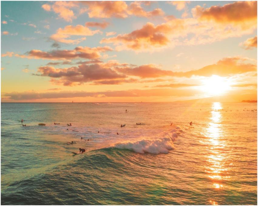 Surfers enjoy vibrant waves under a stunning sunse