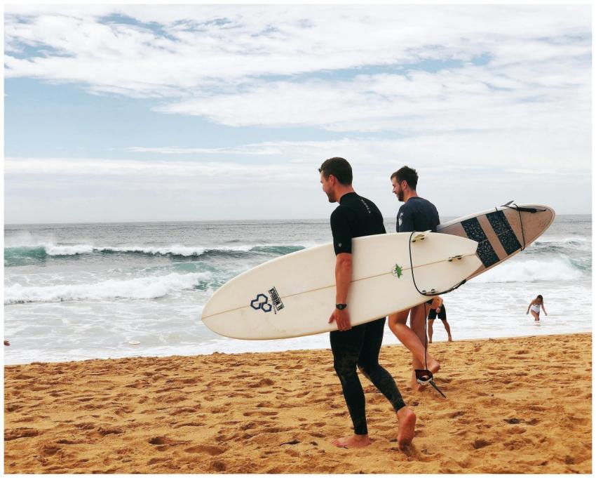 Two men with surfboards walking along Avoca Beach,
