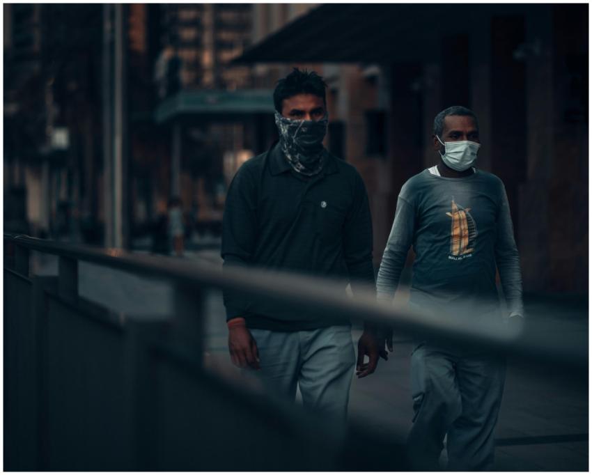 Two men wearing masks walk through a dimly lit str
