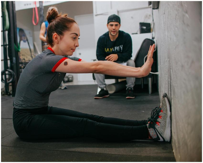 Woman stretching in a gym setting under trainer's