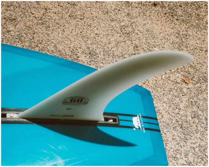 Detailed view of a surfboard fin on a sandy beach.