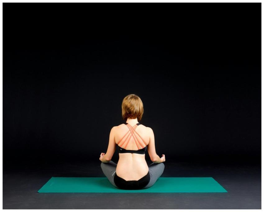 Back view of a woman meditating on a mat in a dark