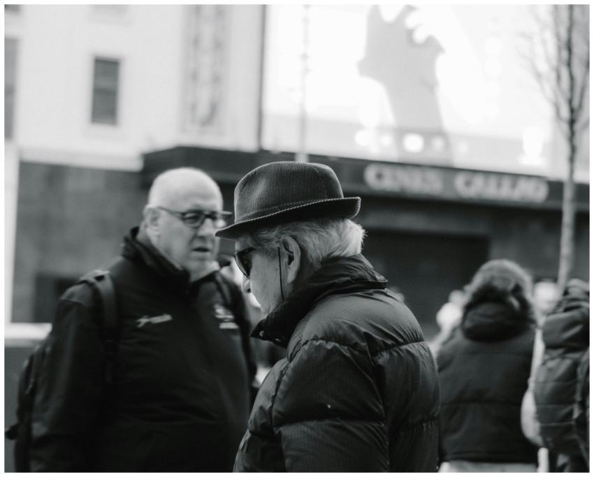 Two elderly men conversing in an urban setting cap