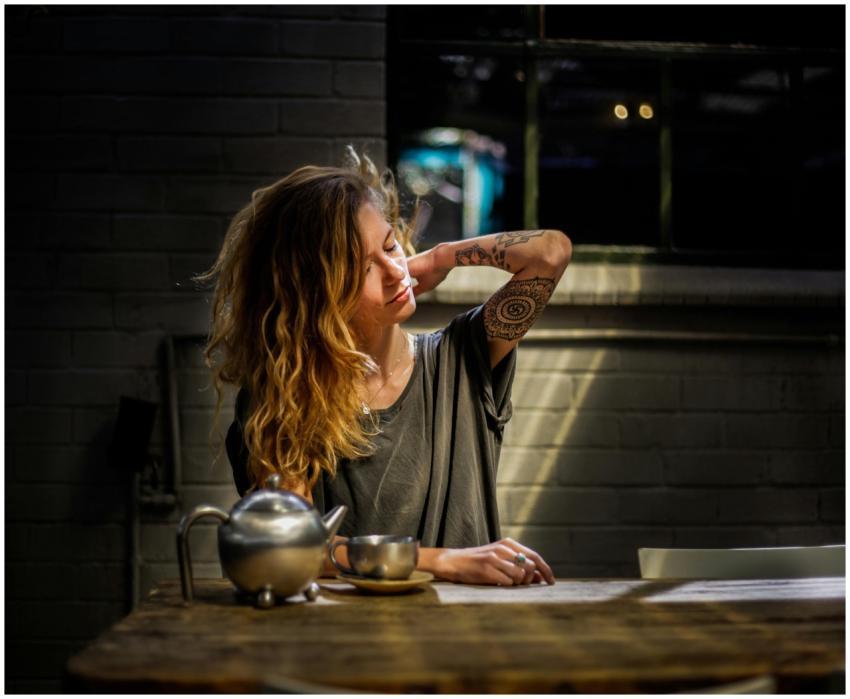 A woman with tattoos relaxes with a cup of tea in