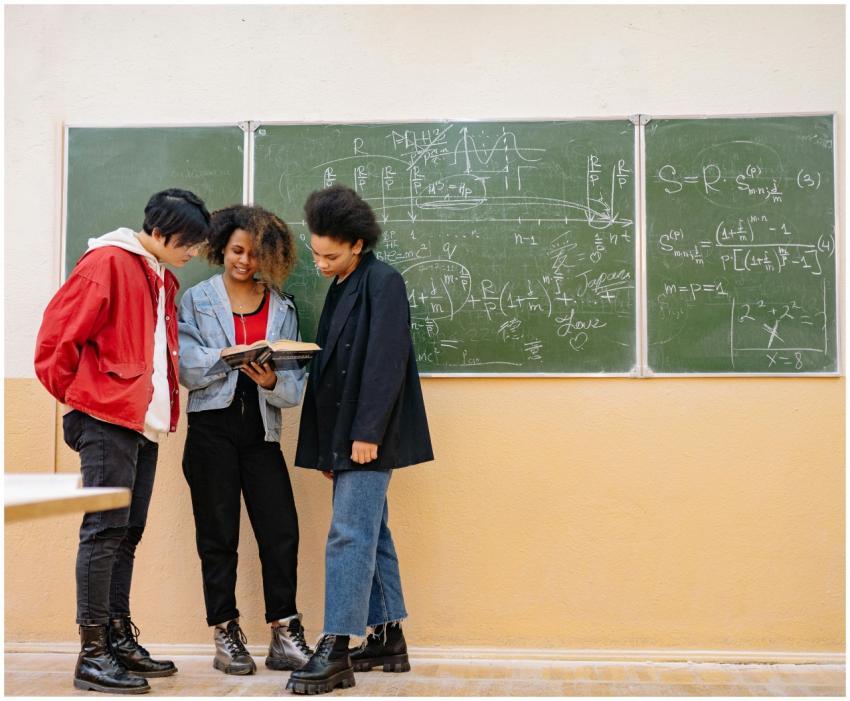 Three diverse students standing by a chalkboard wi