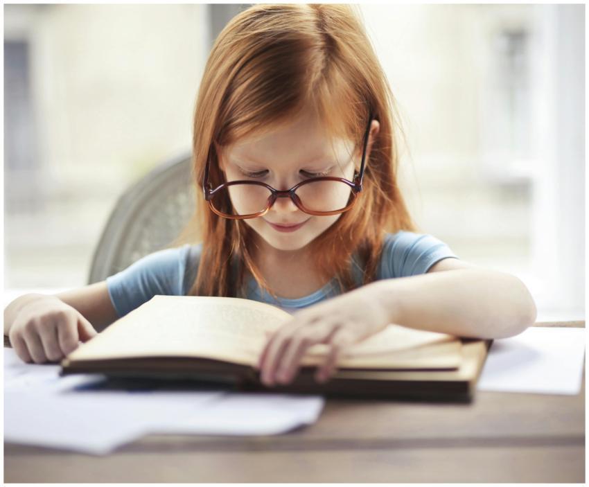 A young girl with glasses intently reads a book in