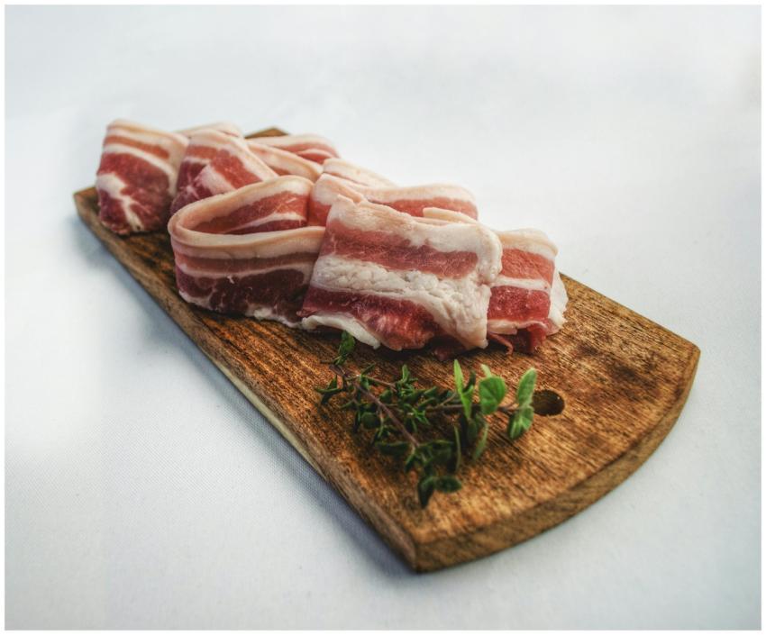 Sliced bacon laid on a rustic wooden board with he