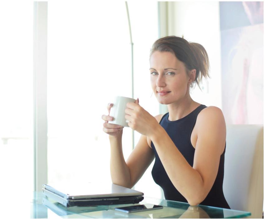 Young woman sitting at her desk, holding a coffee