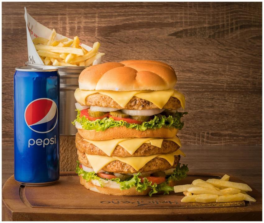 Appetizing triple cheeseburger with fries and Peps
