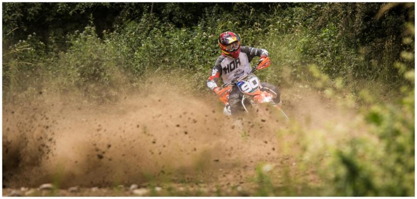 Motocross biker speeds through a dusty dirt track