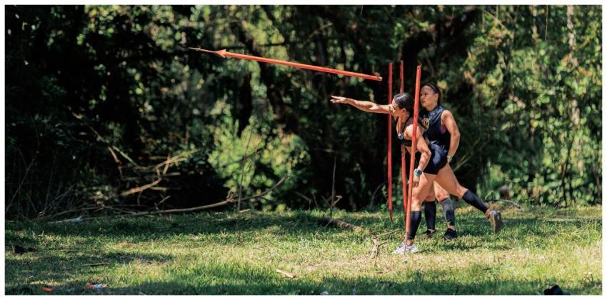 Two women practicing javelin throw outdoors in a l