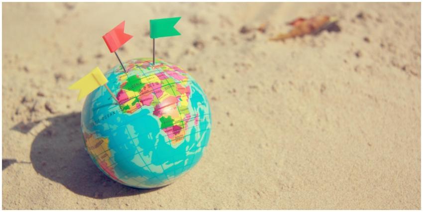 A vibrant globe with pins on a sandy surface, symb