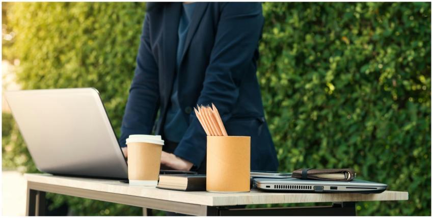 A person working outdoors with a laptop, coffee, a