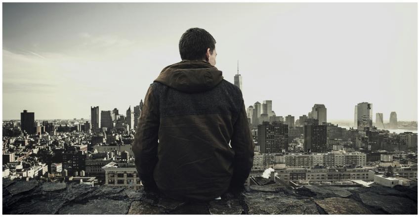 Man sitting on rooftop overlooking city skyline, c