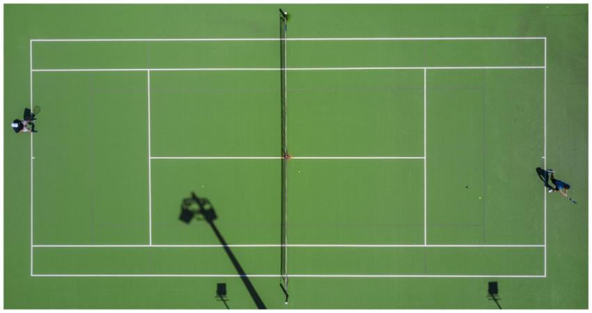 High-angle drone shot of a tennis match on a brigh