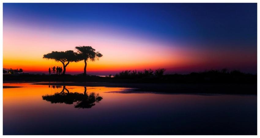 Vibrant sunset with silhouettes reflected in calm