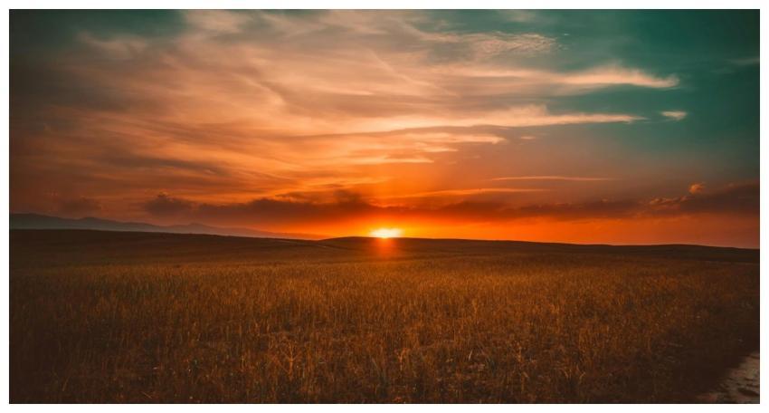 Serene sunset over a vast field with dramatic skie