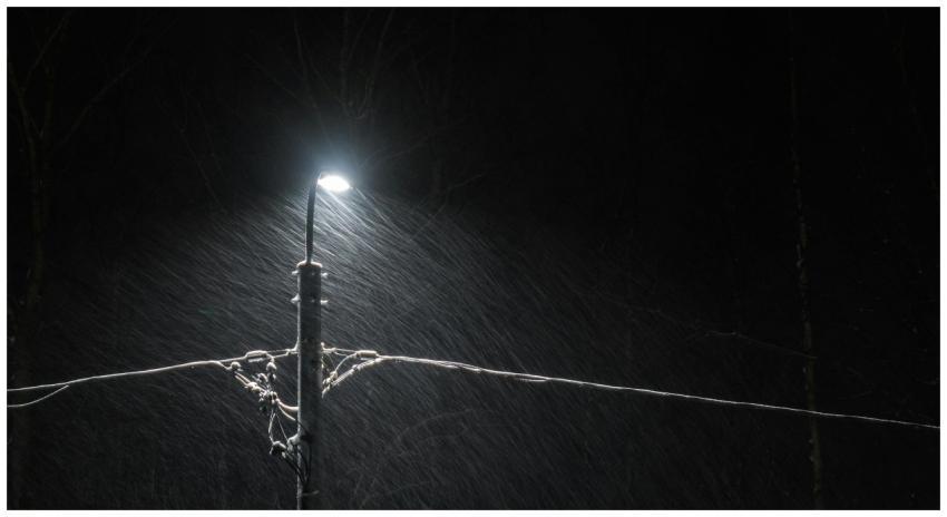 A streetlamp casts light on falling snow in a dark