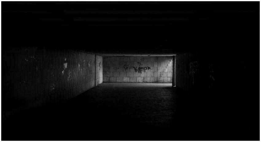 A dimly lit tunnel with graffiti and concrete wall