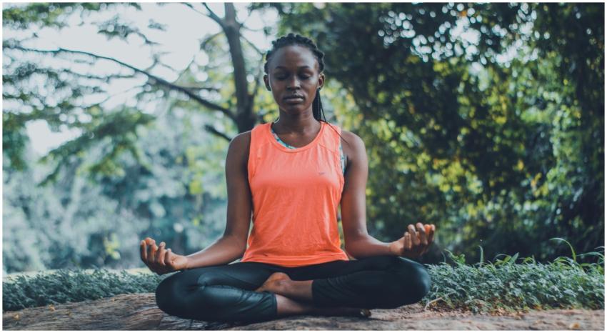 A woman meditating peacefully outdoors in a lush g