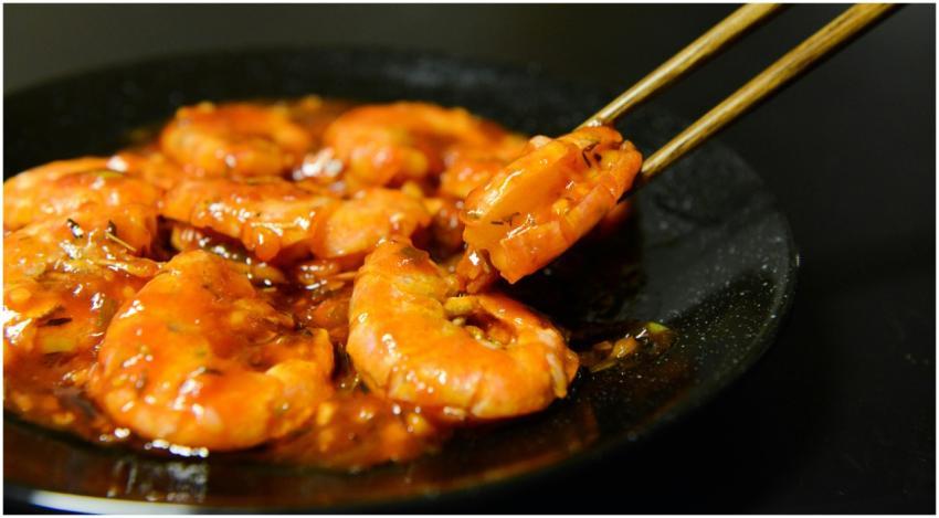 Close-up of spicy prawns in sauce with chopsticks