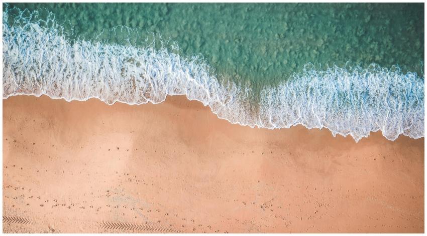 Aerial view of gentle waves meeting sandy beach on