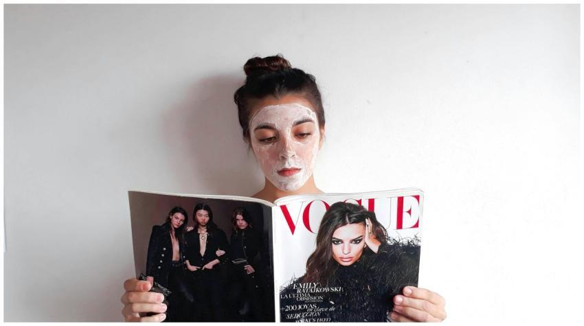Woman with facial mask reads a Vogue magazine, enj