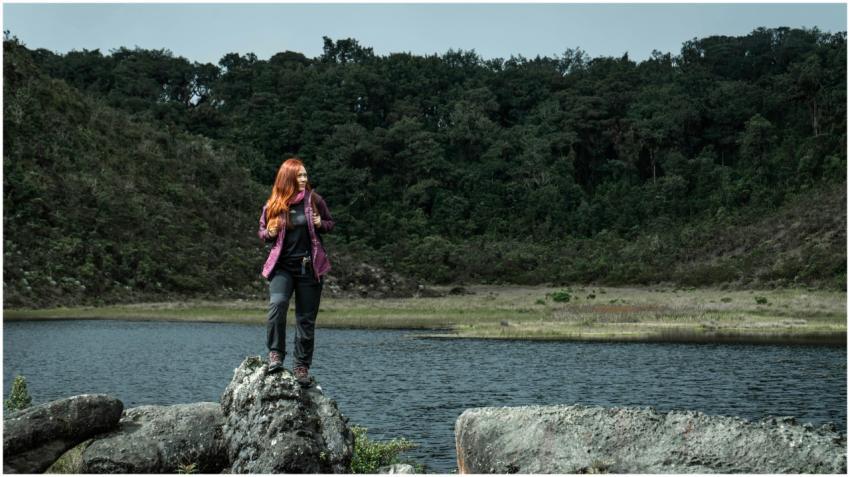 Redhead woman hiking and standing on rocks by a fo