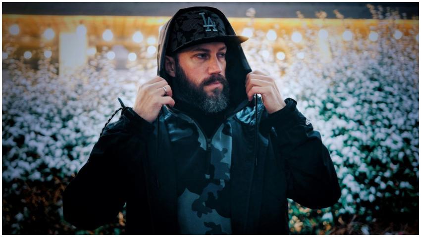 A fashionable man adjusts his black hoodie and cap