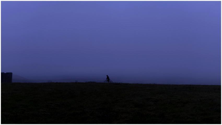 A lone cyclist rides in silhouette against a foggy
