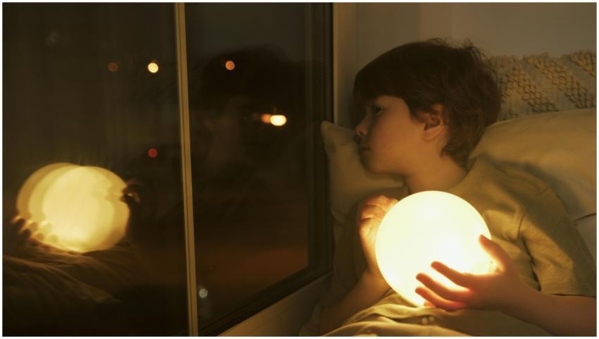 A young boy holding a glowing orb, looking out a w