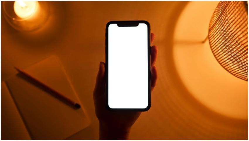 A hand holds a smartphone with a blank screen, ill