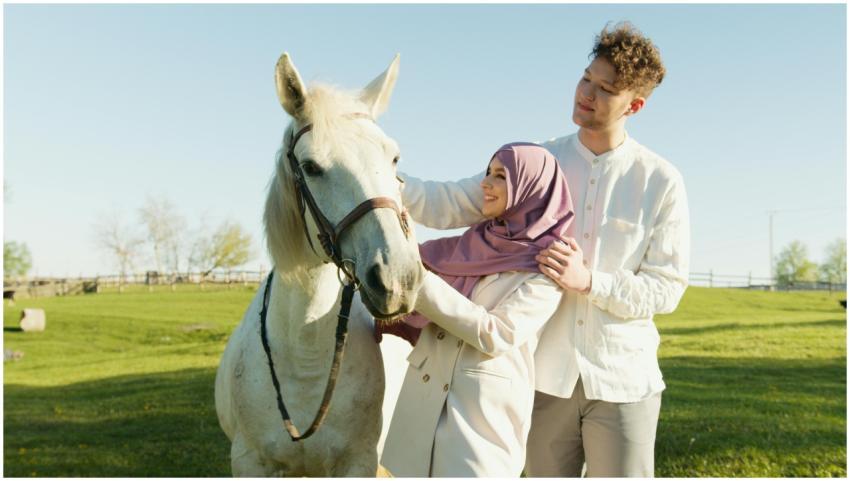 A smiling couple bonding with a white horse on a s