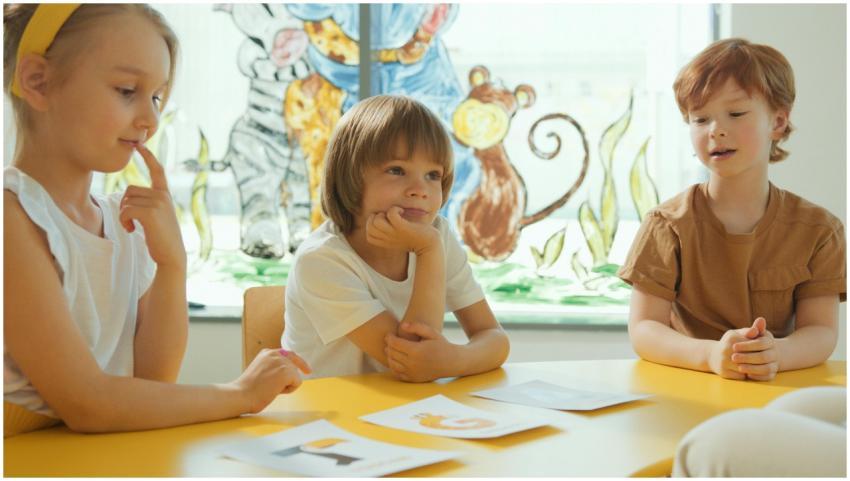 Three children sitting at a yellow table in a clas
