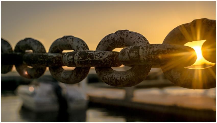 Close-up of a rusty chain with sunrise and water r