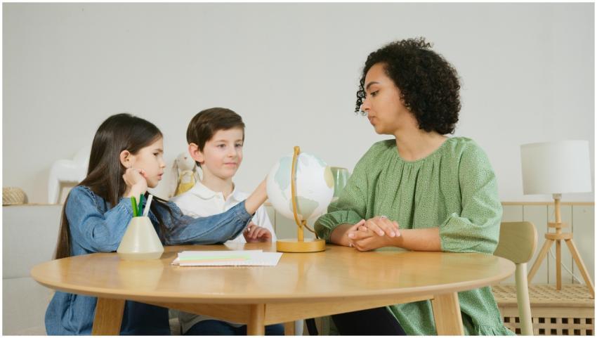 A teacher guides two children in a geography lesso
