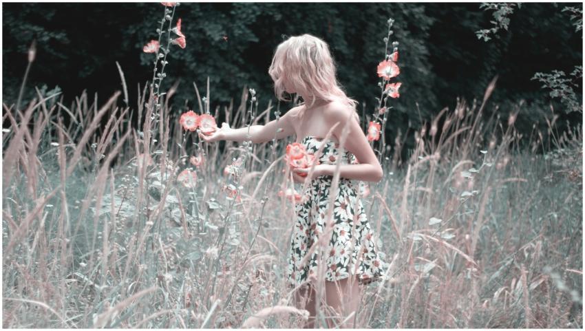 A blonde woman in a floral dress admires flowers i