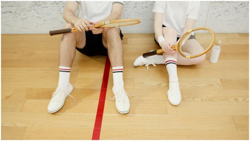 Two young adults sitting with vintage tennis racke