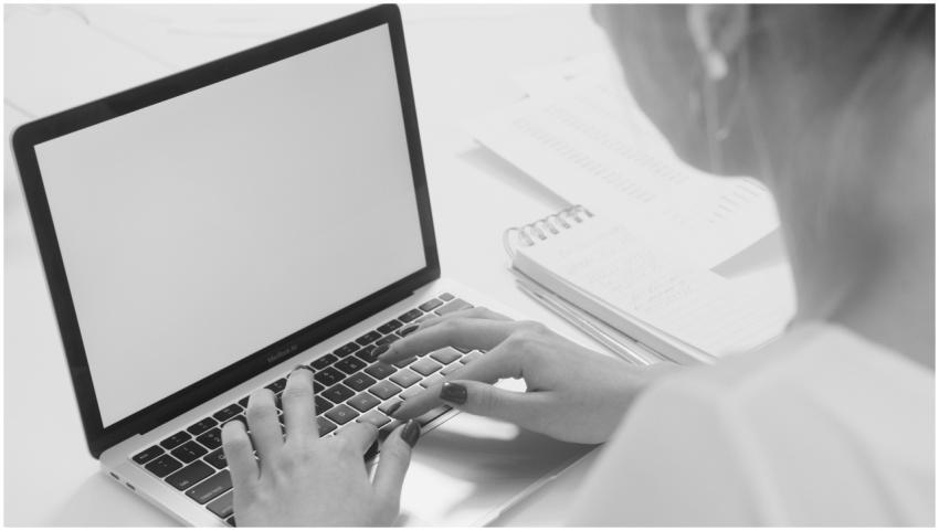 Monochrome image of a person typing on a laptop wi