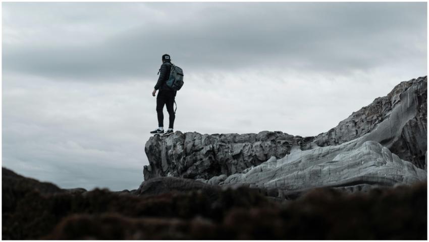 A lone hiker stands at the edge of a rugged cliff