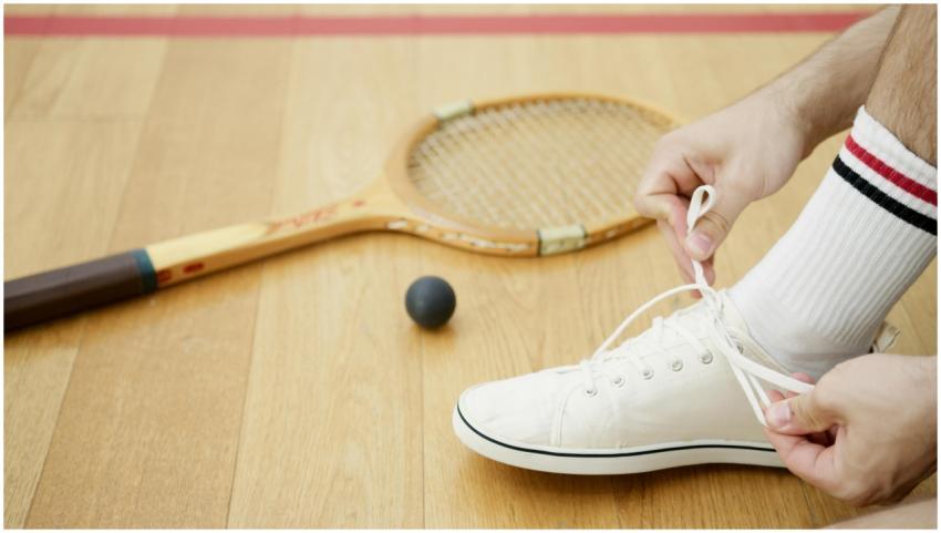 Person tying white sneakers on wooden floor beside