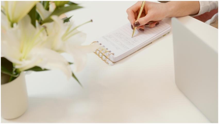 A workspace with lilies, notepad, and gold pen on