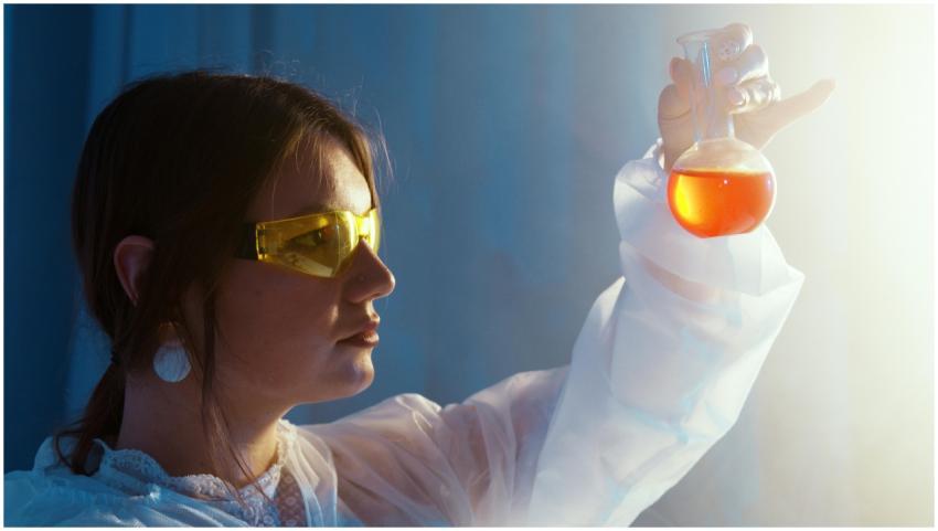 Woman in lab coat examining a vibrant liquid in a